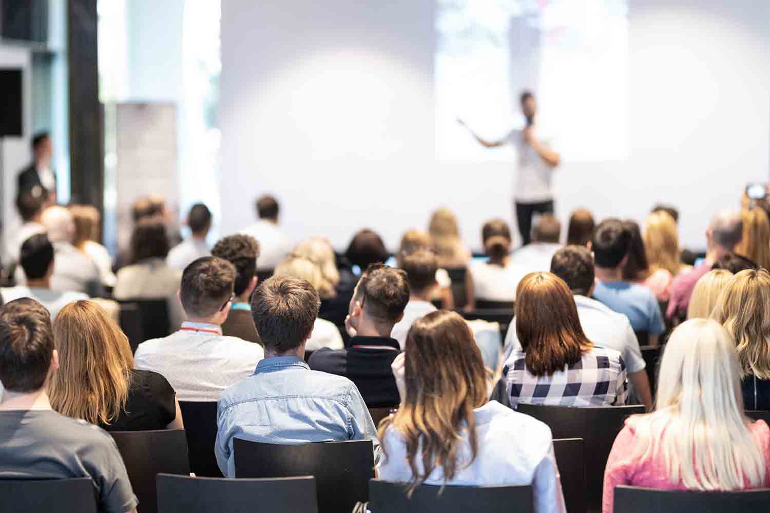Speaker giving a talk in conference hall at business event. Audience at the conference hall. Business and Entrepreneurship concept. Focus on unrecognizable people in audience.